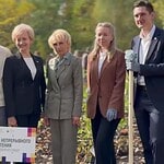 Четыре участника мероприятия позируют с лопатами у посадок.