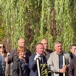 Группа участников с лопатами стоит среди молодых посадок.