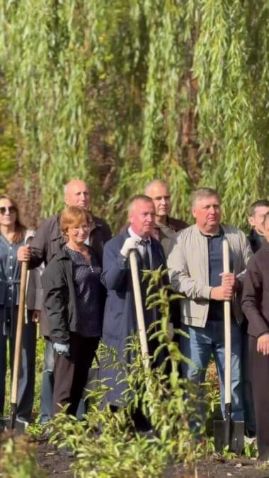 Группа участников с лопатами стоит среди молодых посадок.