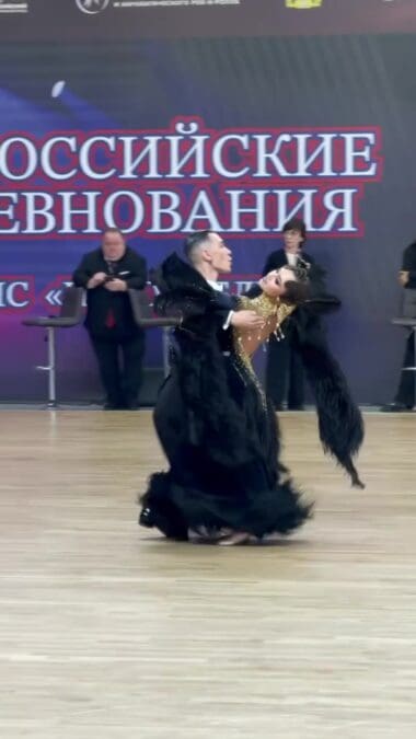 Мужчина поддерживает партнёршу в чёрном платье во время танца.