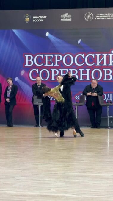 Танцевальная пара выступает на паркете перед баннером всероссийских соревнований.