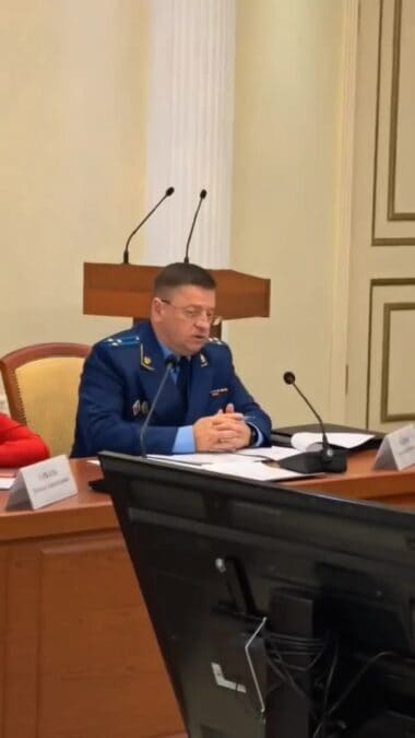 Мужчина в синем форменном кителе сидит за столом с документами.
