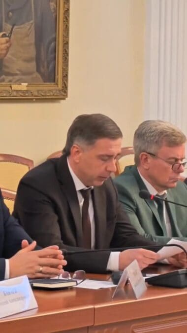 Двое мужчин читают документы и выступают в ходе заседания.