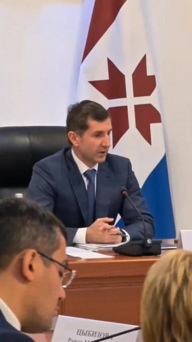 Мужчина в костюме выступает за столом на фоне флага Мордовии.