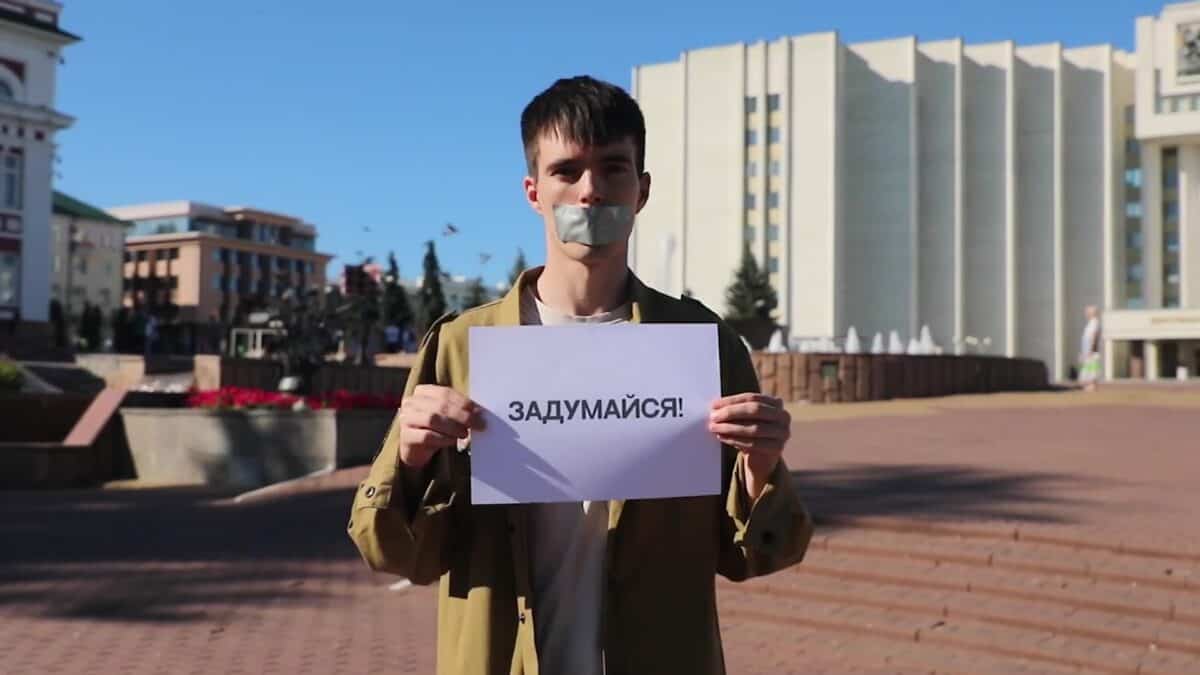Молодой человек с заклеенным ртом держит плакат с надписью «Задумайся!».