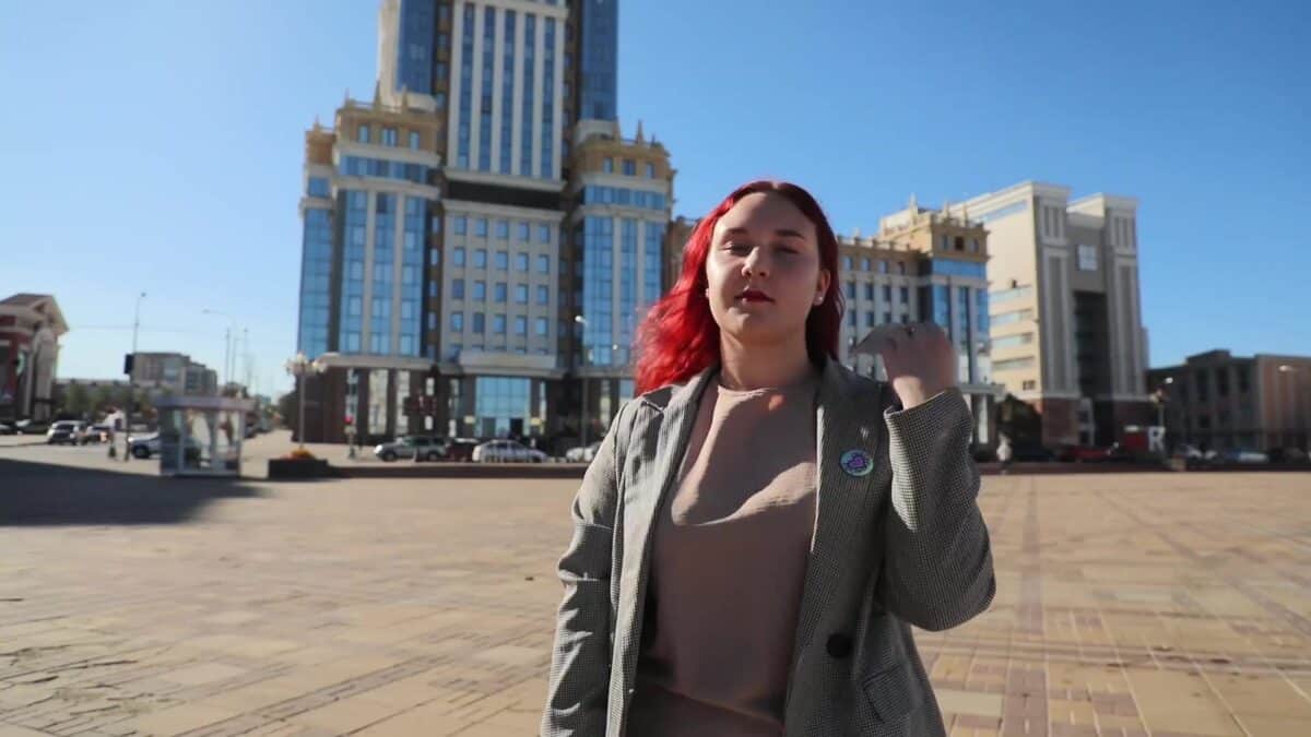 Девушка стоит на городской площади на фоне высоких зданий.
