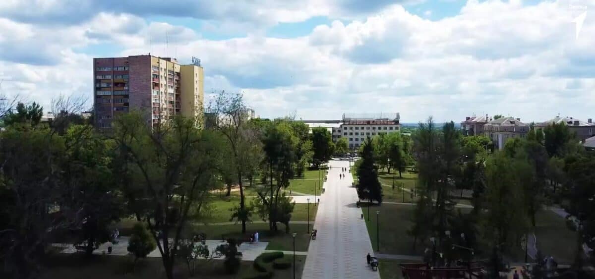 Аллея городского парка ведёт к зданиям среди деревьев.
