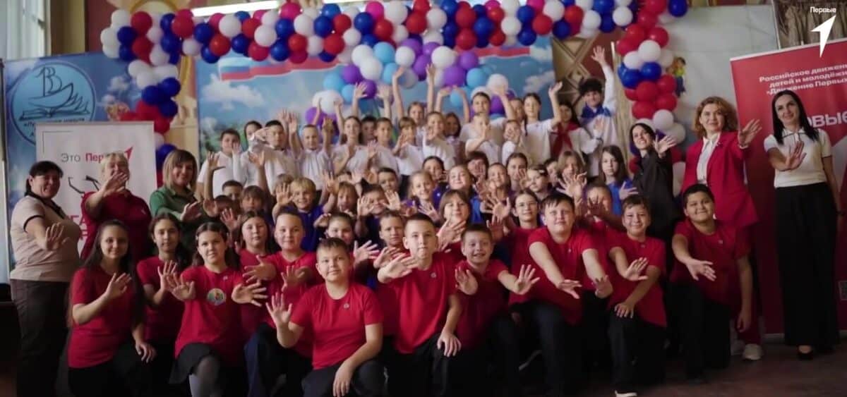 Большая группа детей и взрослых позирует в зале с воздушными шарами.