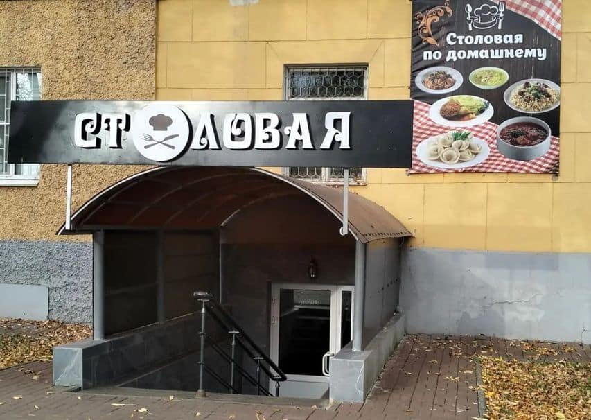 Вход в столовую с чёрной вывеской и рекламным баннером блюд.