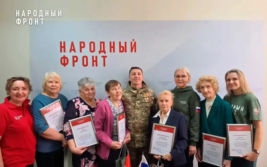 Группа женщин с благодарственными грамотами стоит у стенда Народного фронта.