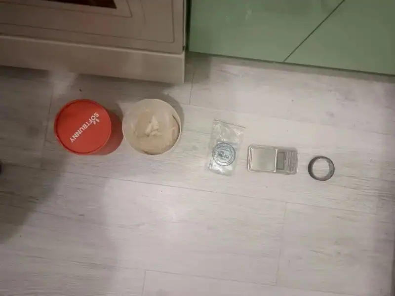 На полу разложены электронные весы, пакет с белым веществом и упаковочные предметы.