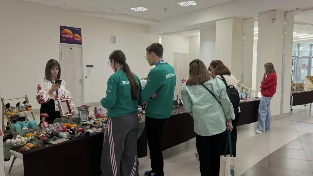 Посетители в зелёных толстовках рассматривают товары у прилавка.