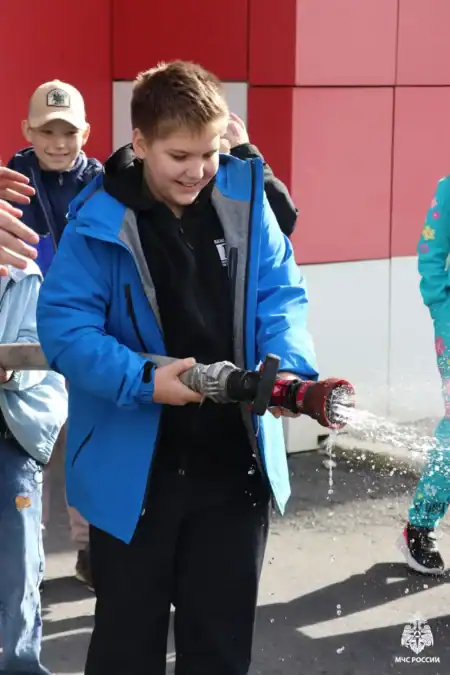 Мальчик держит пожарный ствол, из которого льётся вода.