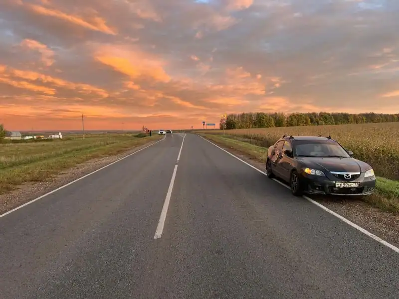 Чёрная Mazda стоит на обочине загородной дороги на закате.