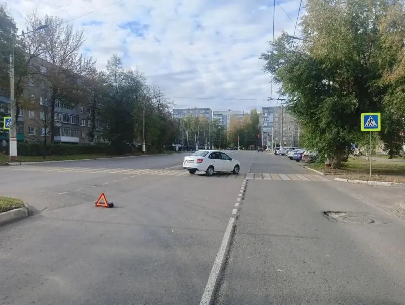 Белый автомобиль стоит у пешеходного перехода, на дороге установлен аварийный треугольник.