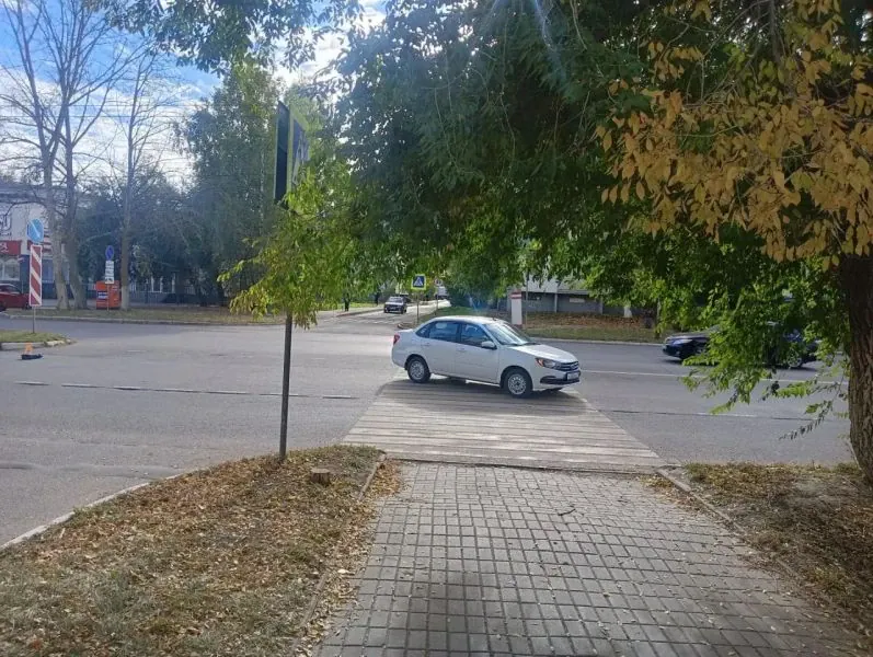 Белый автомобиль находится рядом с пешеходным переходом на городской улице.
