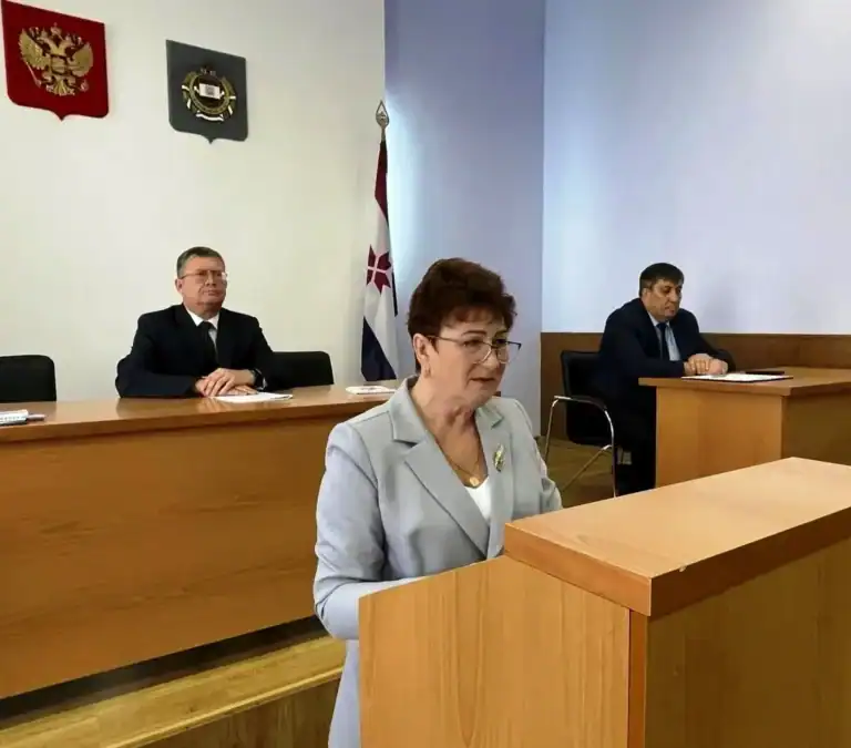 Женщина выступает за трибуной перед членами президиума.