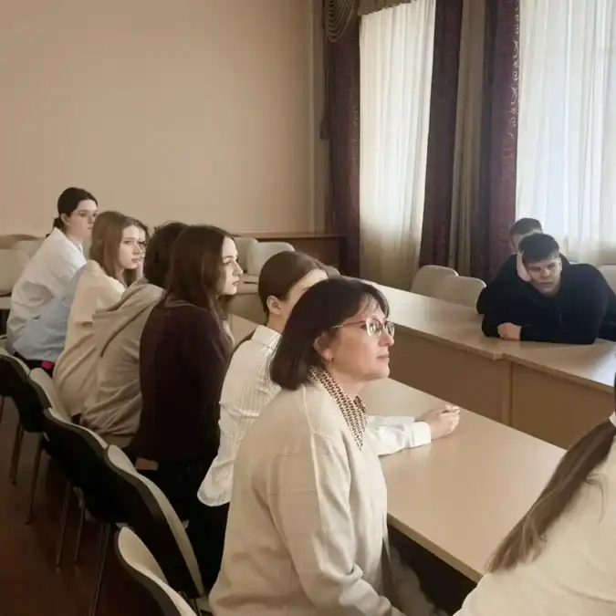 Школьники и взрослая женщина сидят за партами в аудитории.