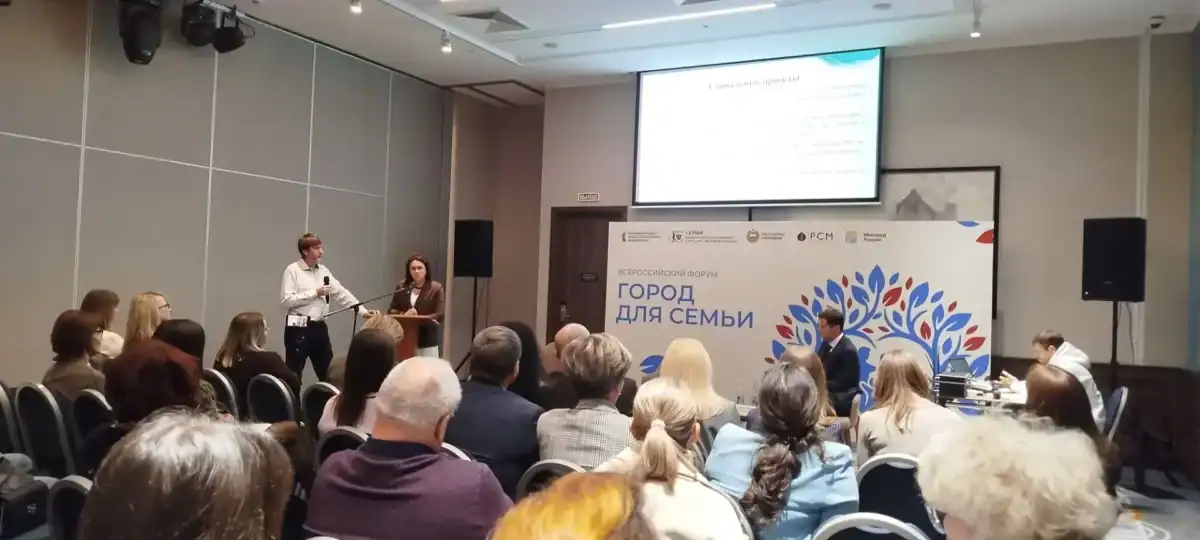 Мужчина выступает у трибуны перед заполненным залом участников форума.