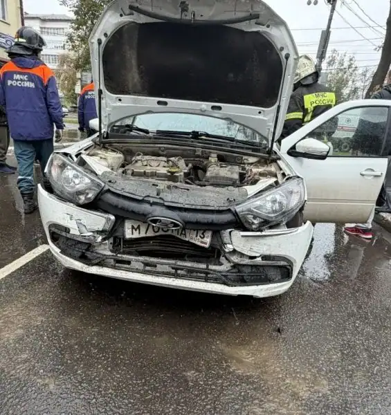 Повреждённая белая Lada с открытым капотом и сотрудниками МЧС рядом.