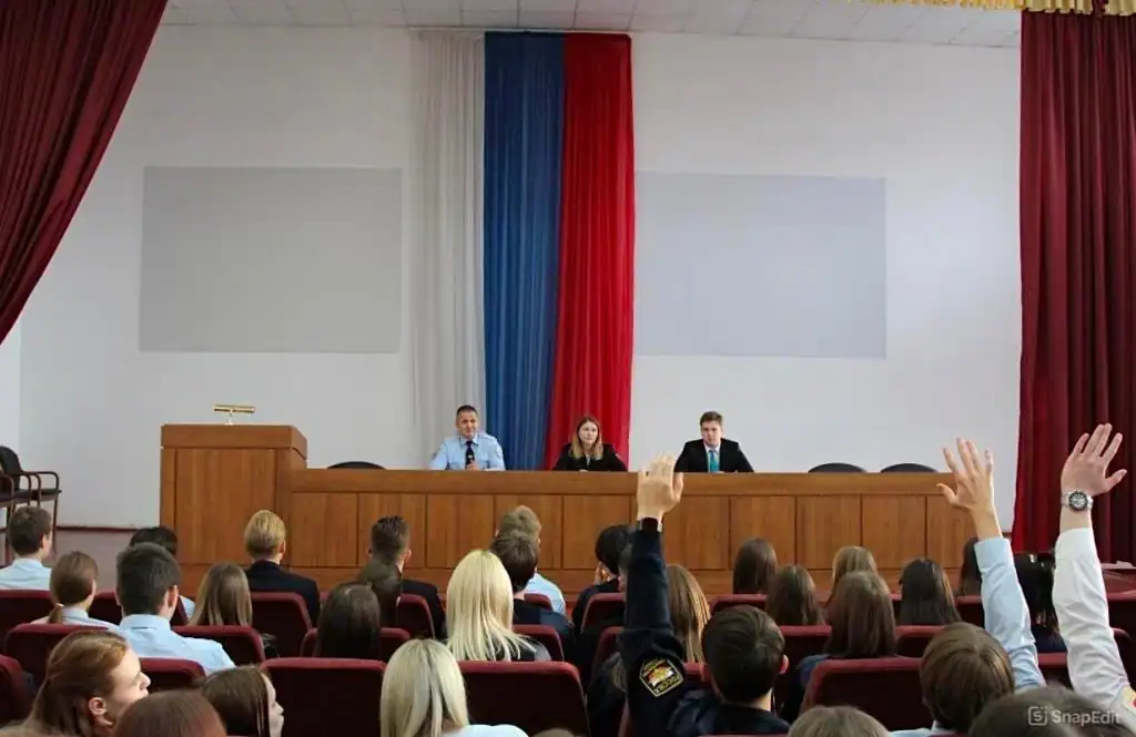 Студенты в актовом зале поднимают руки перед тремя спикерами за столом.