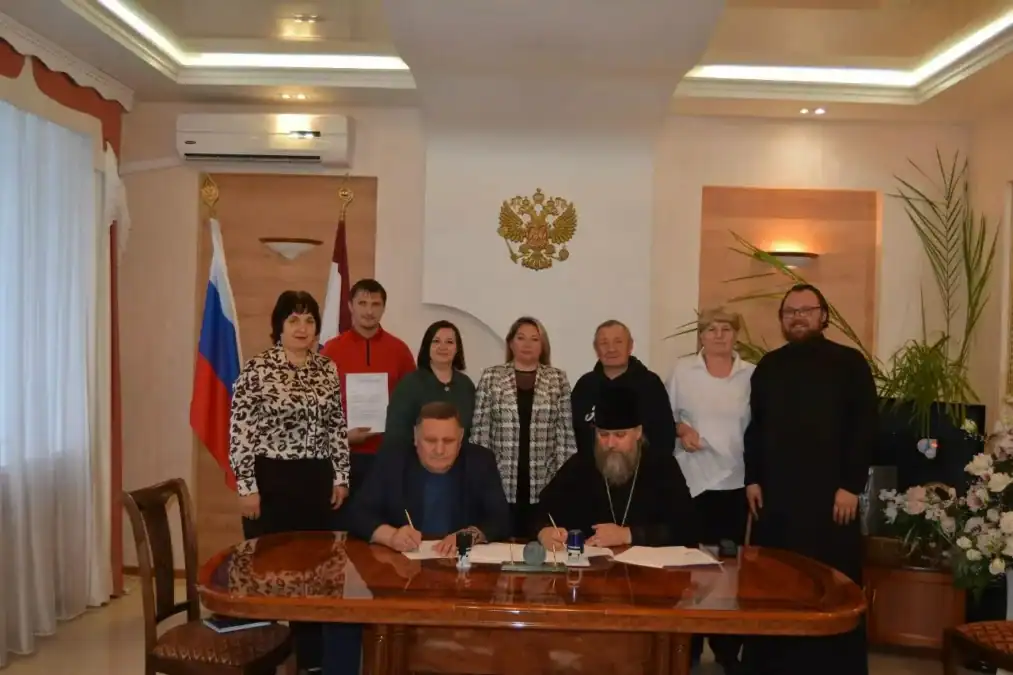 Двое мужчин подписывают документы за столом в присутствии участников встречи.