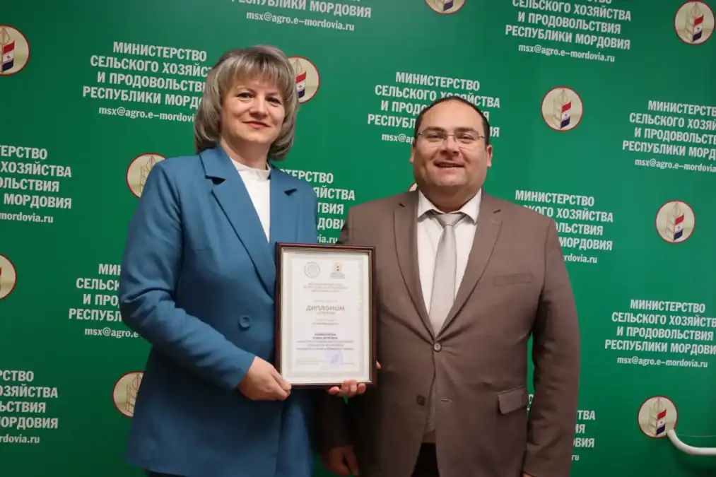 Женщина в голубом костюме держит диплом рядом с мужчиной.