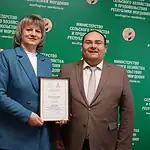 Женщина в голубом костюме держит диплом рядом с мужчиной.