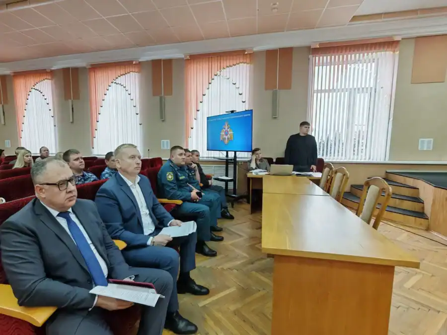 Участники заседания сидят в зале, перед ними установлен экран с эмблемой.