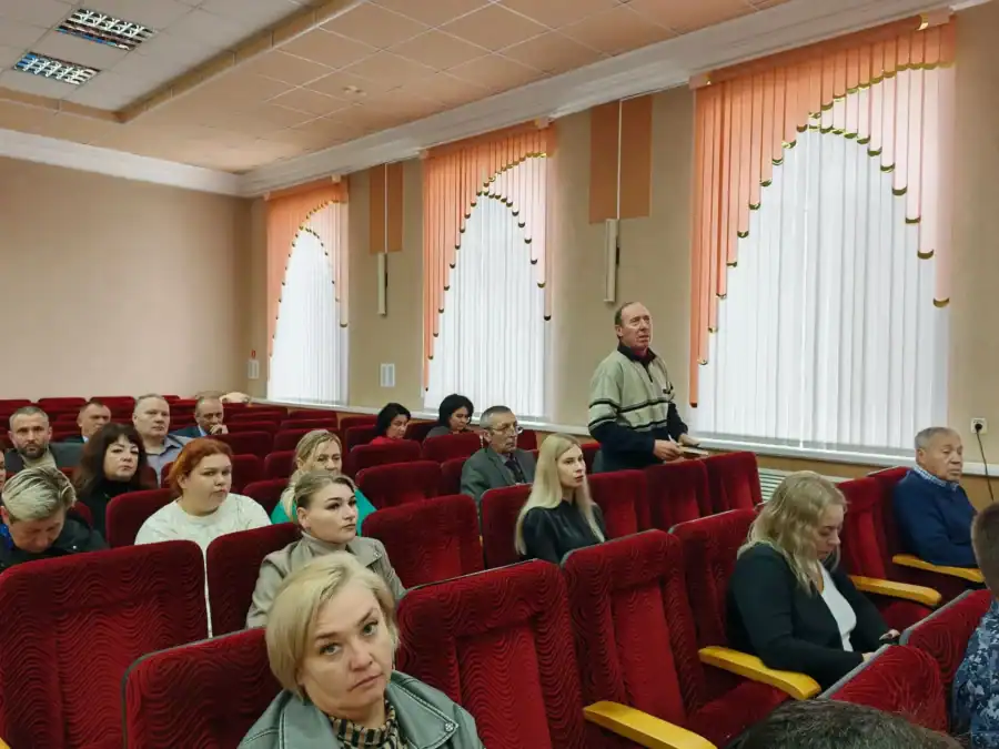 Собравшиеся занимают кресла в зале, один мужчина стоит у своего места.