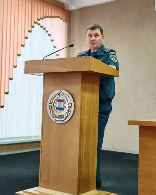 Сотрудник в форме выступает с трибуны, украшенной гербом.