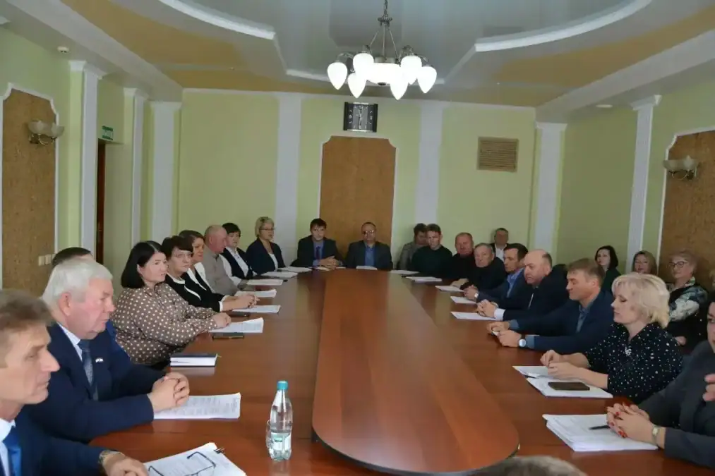 Участники заседания сидят за длинным столом с документами.