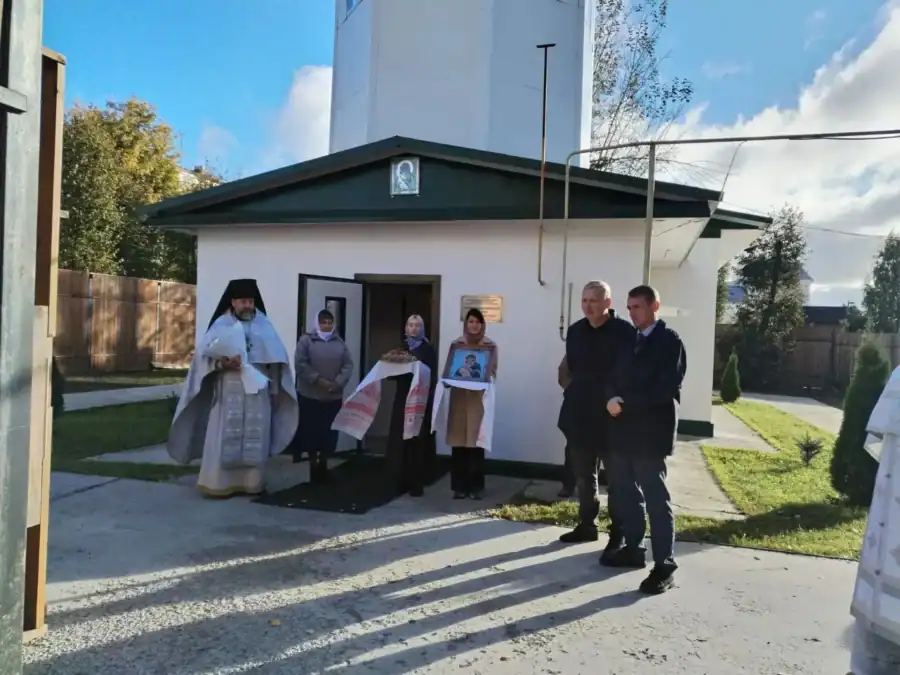 Священнослужители и прихожане стоят у входа в небольшое храмовое здание.
