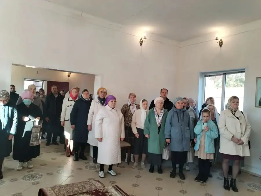 Группа прихожан, включая ребёнка, стоит в помещении с белыми стенами.