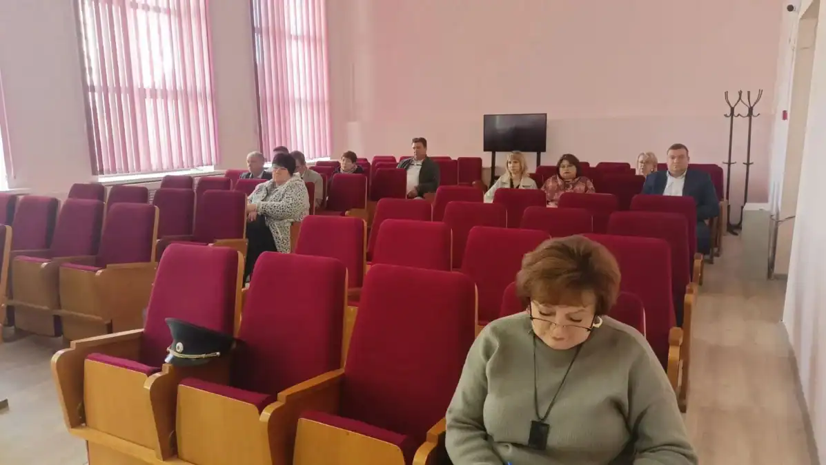 Участники заседания сидят в зале с рядами красных кресел.