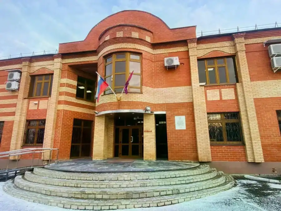 Вход в кирпичное административное здание с флагами над крыльцом.