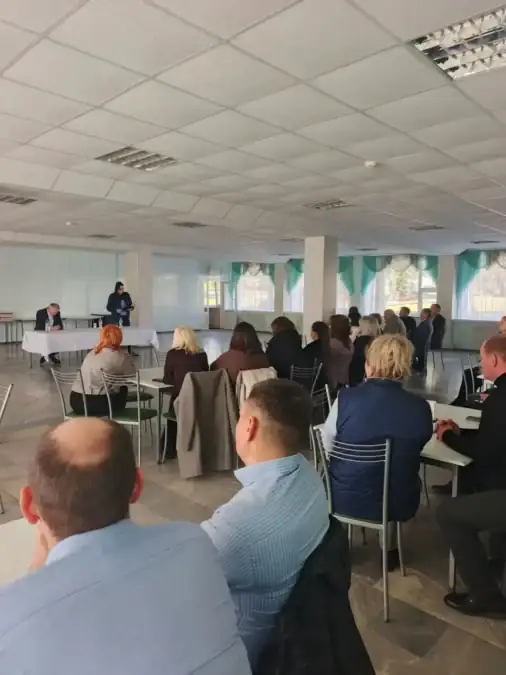 Сотрудница выступает перед сидящими участниками встречи в светлом зале.