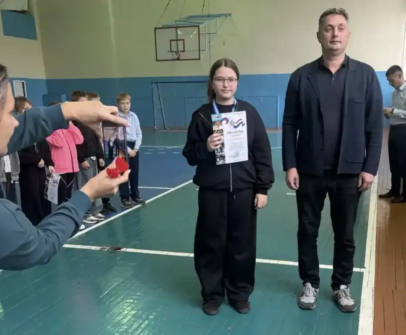 Девушка с медалью держит диплом рядом с мужчиной в спортивном зале.