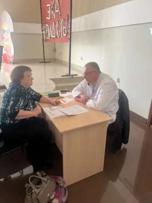 Женщина беседует с врачом за столом, на котором лежат документы.