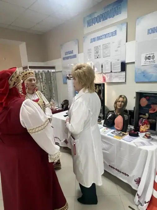 Женщины в народных костюмах общаются у выставочного стола с изделиями.