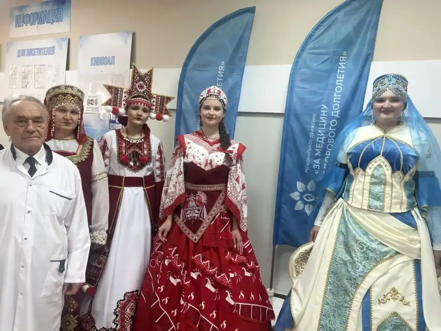 Медработник и женщины в народных костюмах стоят у тематической площадки.