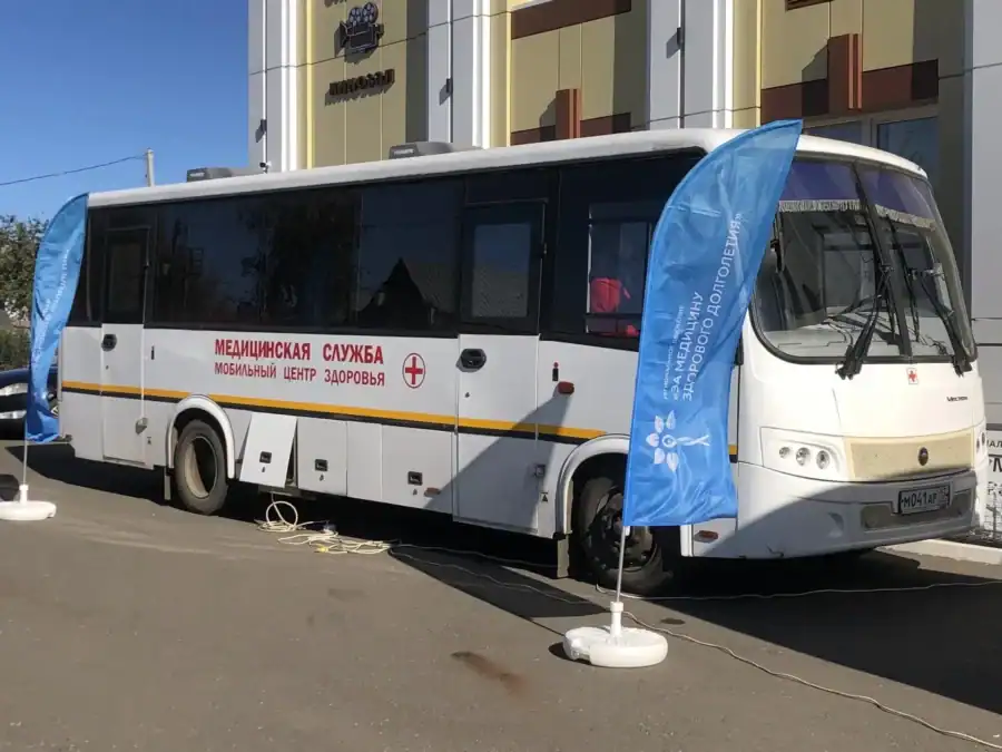 Автобус с надписью о мобильных центрах здоровья припаркован у здания.