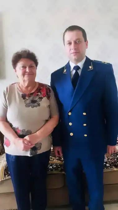 Сотрудник прокуратуры стоит рядом с женщиной в жилой комнате.