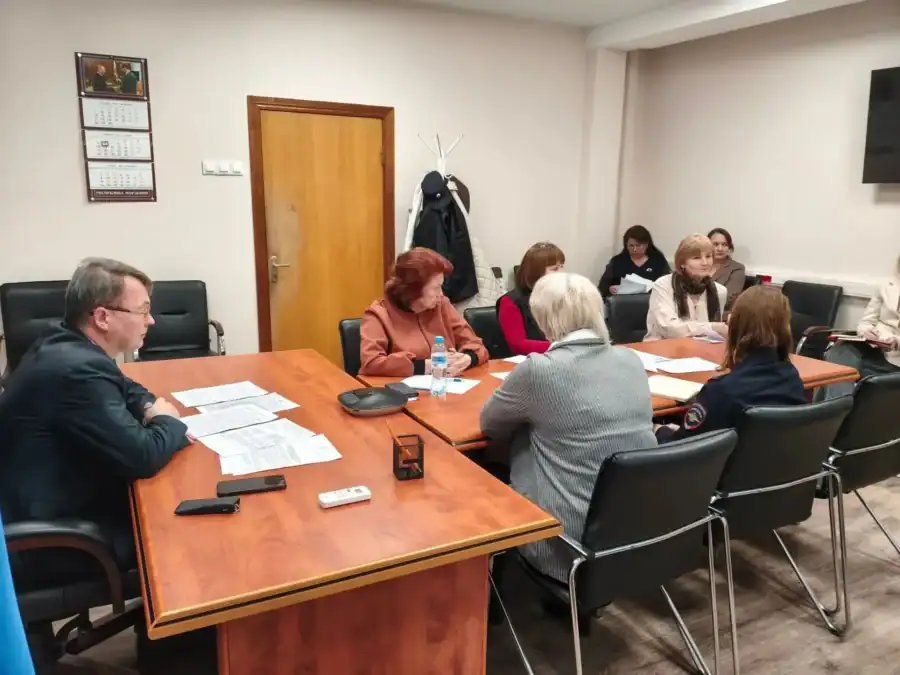 Участники комиссии рассматривают бумаги за длинным рабочим столом.