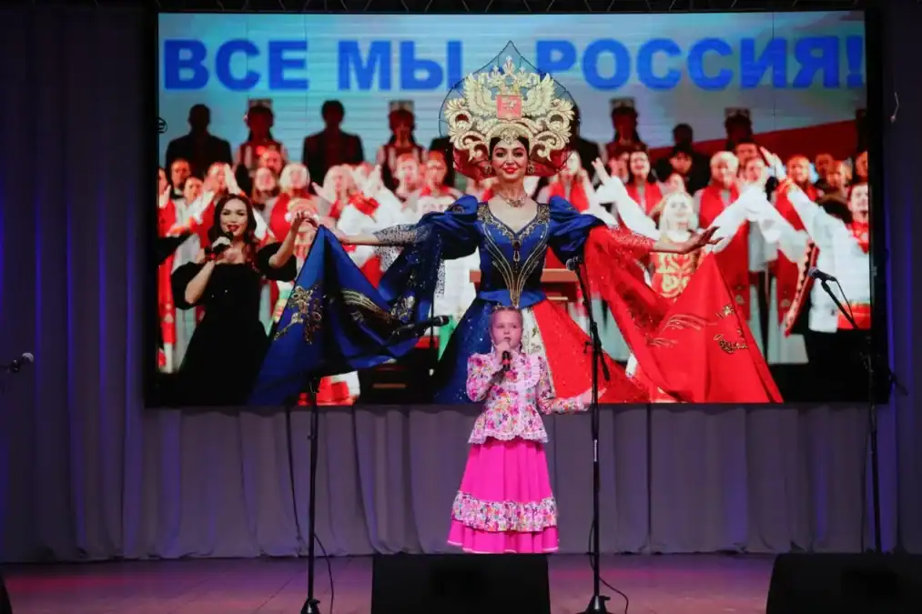 Девочка в розовом народном костюме выступает с микрофоном на сцене.