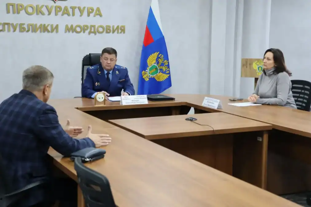 Прокурор и женщина за столом беседуют с мужчиной, пришедшим на прием.