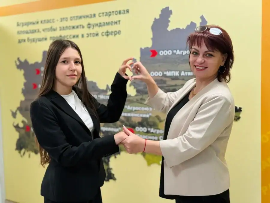 Девушка и женщина соединяют руки на фоне стенда об аграрных классах.