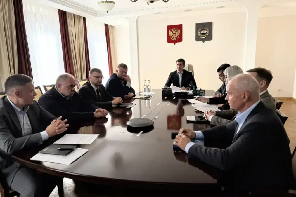 Участники совещания сидят за длинным столом в кабинете.