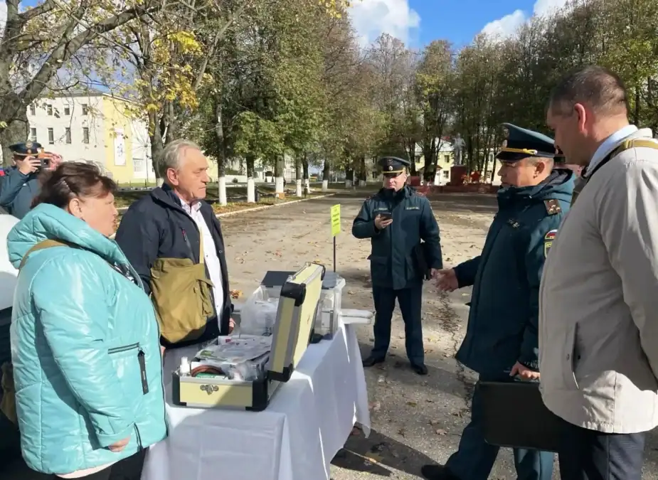 Участники смотра обсуждают оборудование, размещённое на столе под открытым небом.