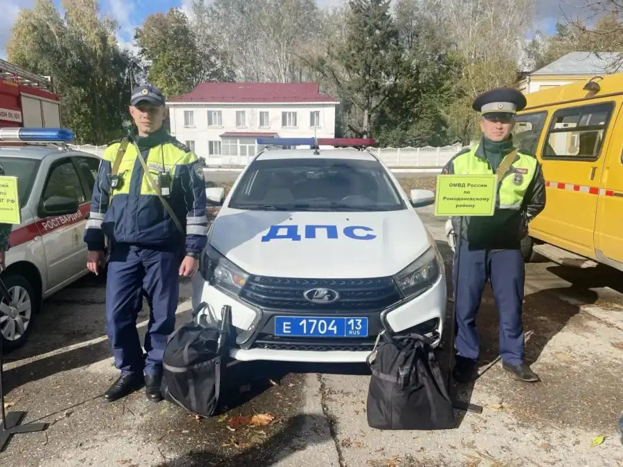 Инспекторы ДПС стоят у патрульного автомобиля с двумя чёрными сумками.